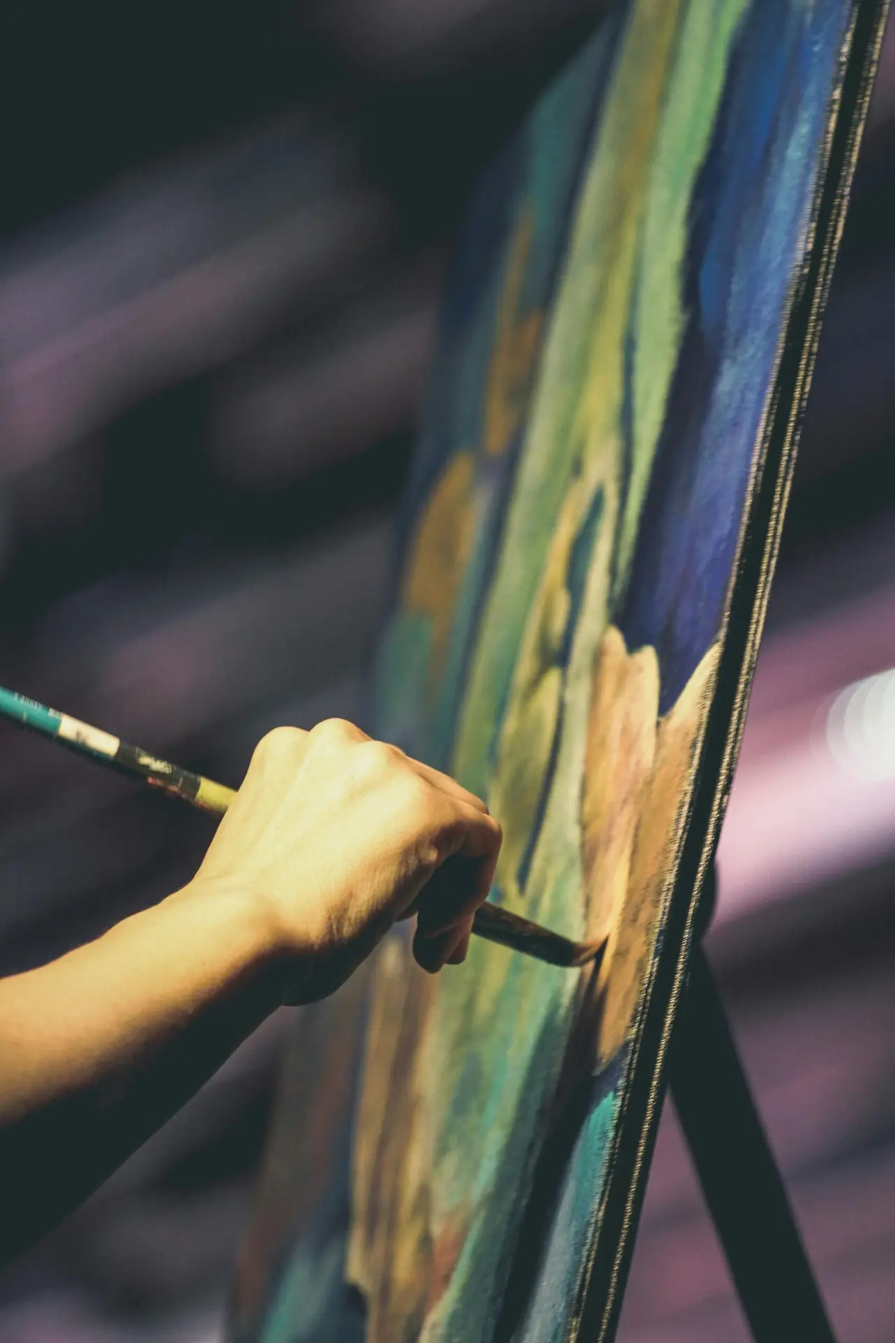 An artist's hand painting a vibrant abstract artwork on a canvas with a brush.